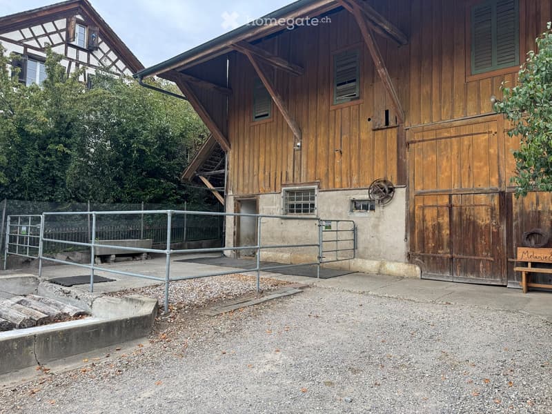 Two-story wooden building with a barn-like structure, metal fence, and small wooden bench.
