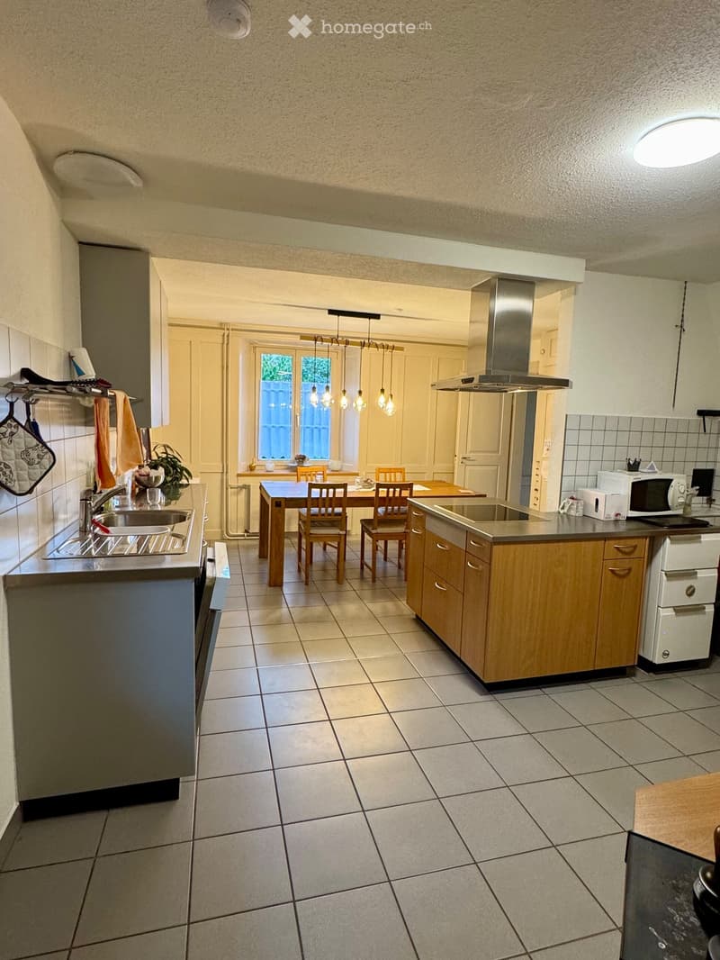 Modern kitchen with tiled floor, wooden cabinets, stainless steel appliances, and a dining area with a table and chairs.