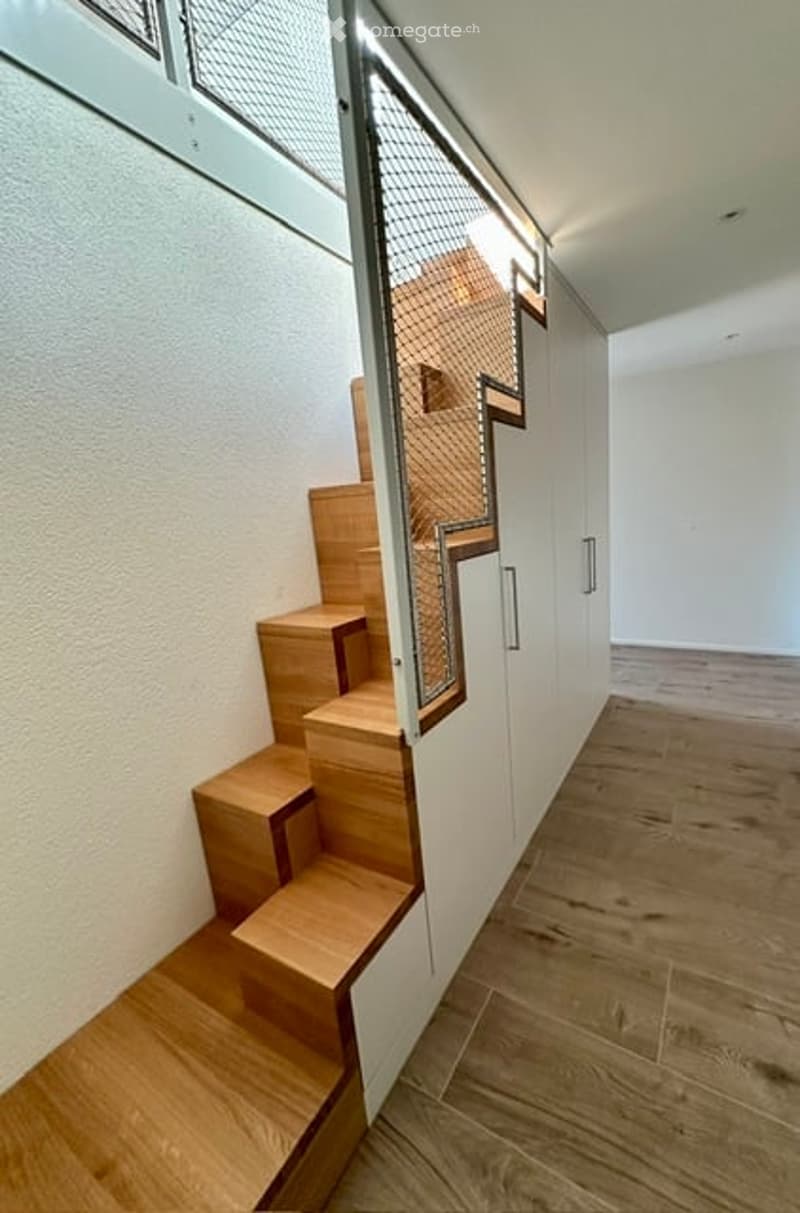 Modern hallway with wooden flooring, white walls, and a staircase with wooden steps and a metal railing.
