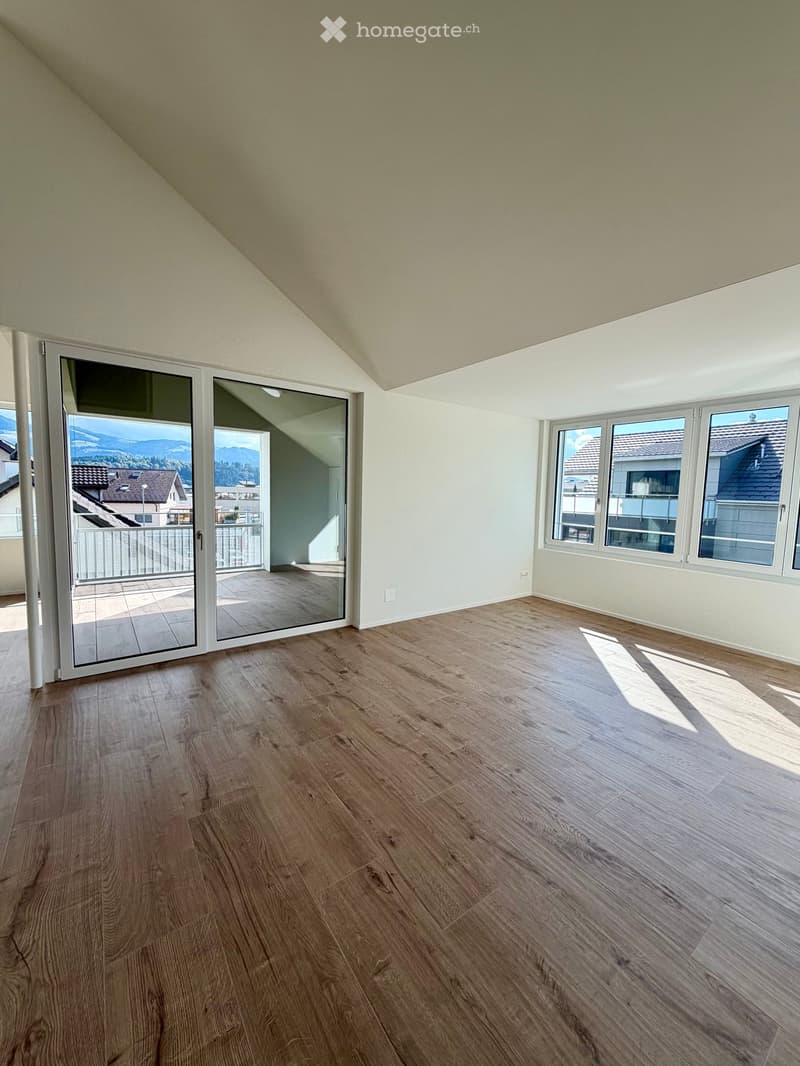 Empty room with wooden flooring, large windows, and a sliding glass door leading to a balcony.