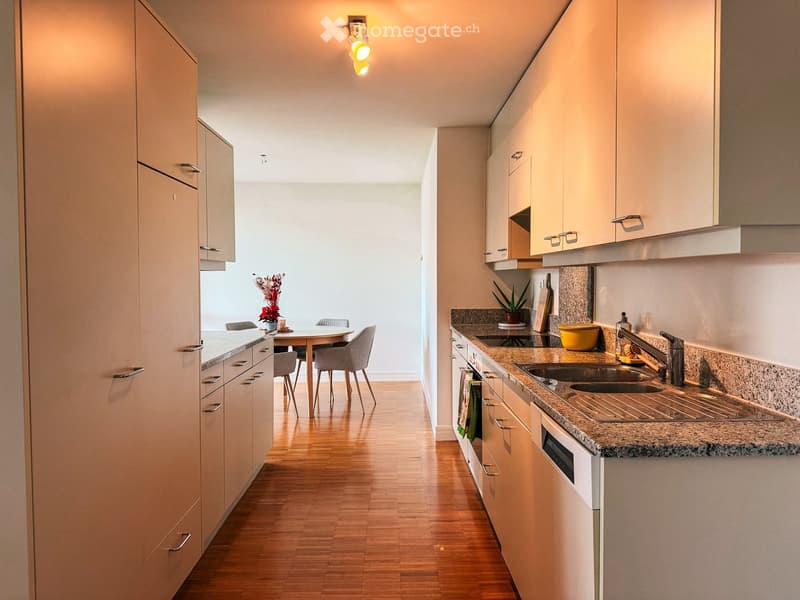 Modern kitchen with light wood cabinets, granite countertops, and a dining area with a table and chairs.
