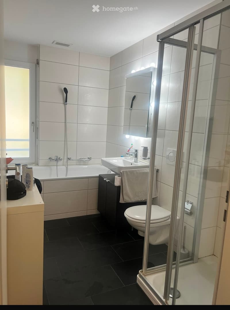 Modern bathroom with white tiles, black floor, bathtub, sink, toilet, shower, and a towel on the sink.