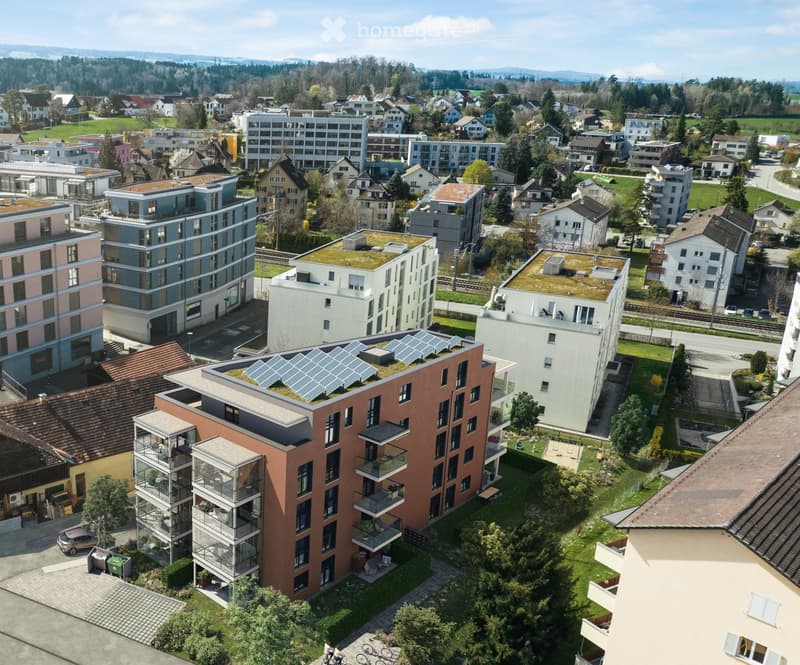 Aerial view of a modern residential area with multiple apartment buildings, green roofs, solar panels, and surrounding greenery.