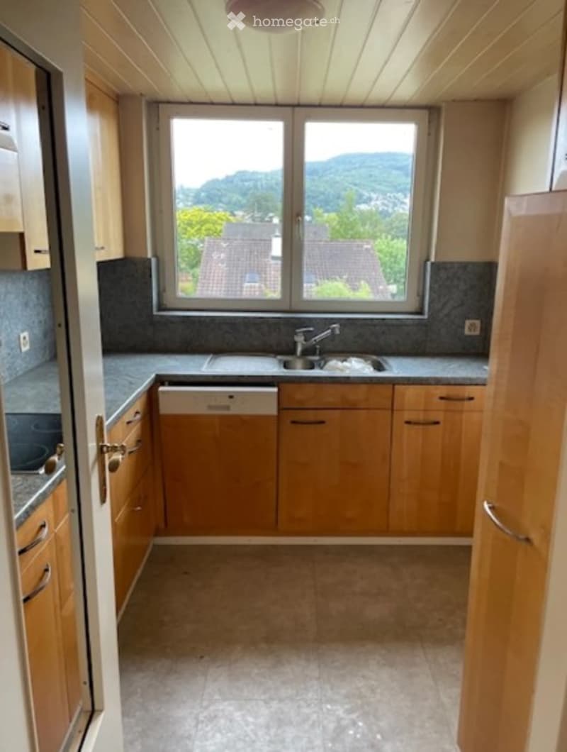 Bright kitchen with wooden cabinets, granite countertops, and a large window offering a scenic view of the surrounding landscape.