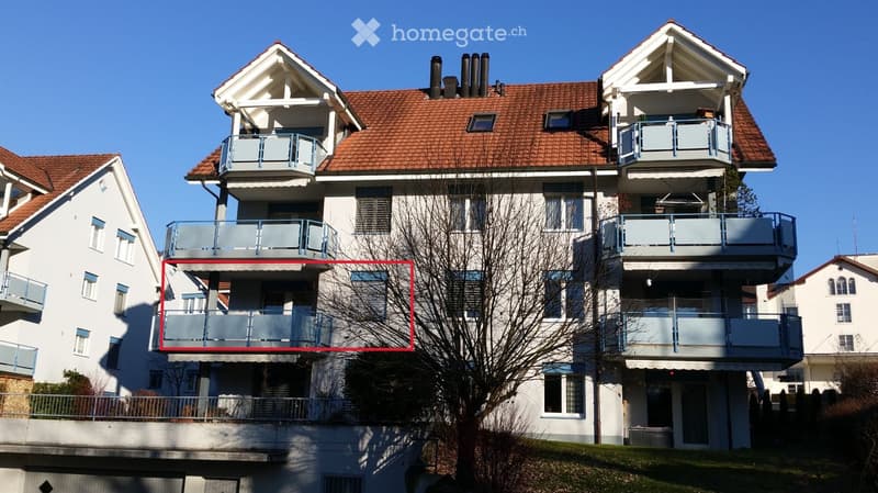 Multi-story residential building with multiple balconies and a red-tiled roof.