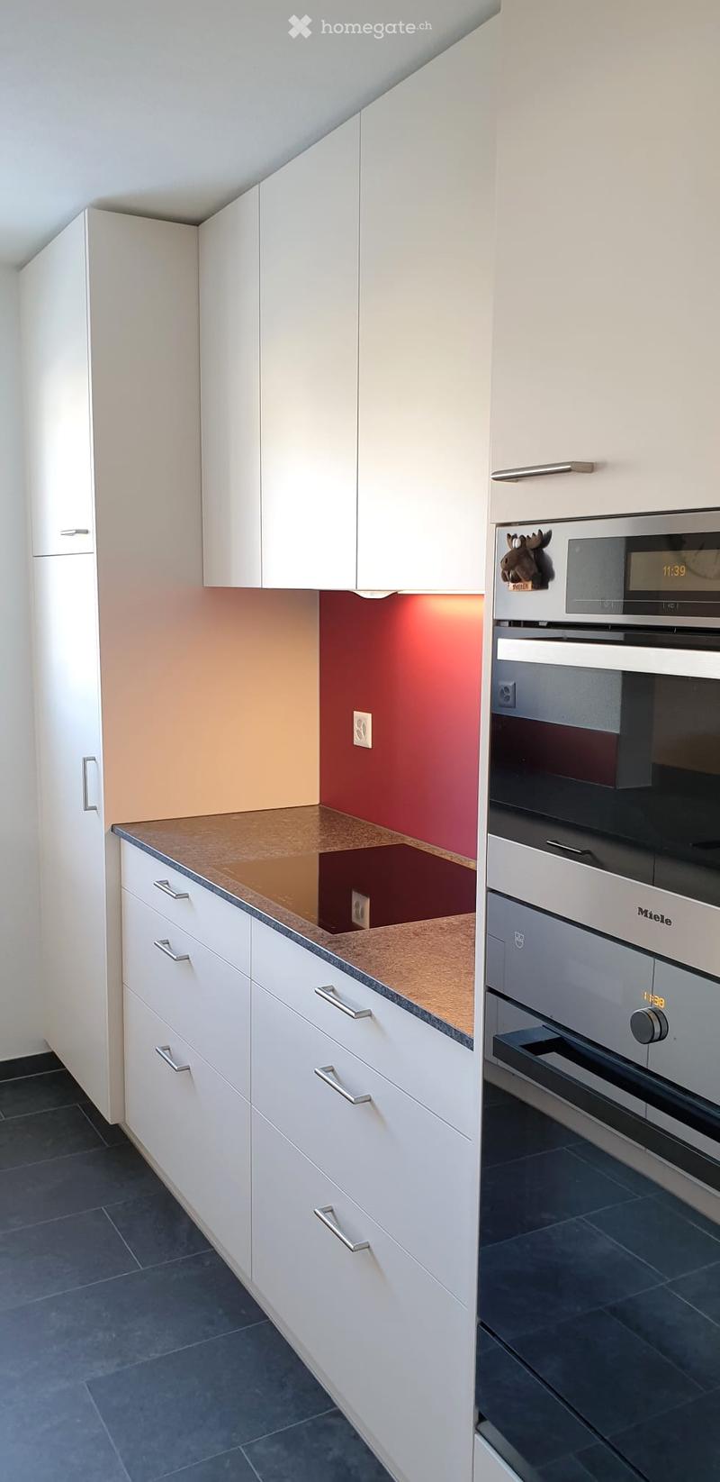 Modern kitchen with white cabinets, a stainless steel oven, and a brown countertop. The walls are painted in a warm, reddish-orange color.