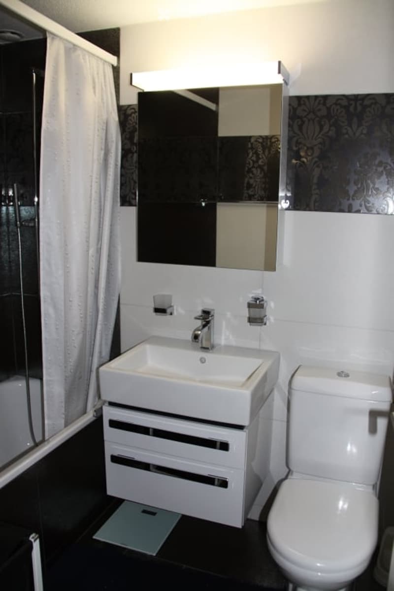 Modern bathroom with a white sink, toilet, and large mirror above the sink. The walls are white with black accents, and the floor is black.