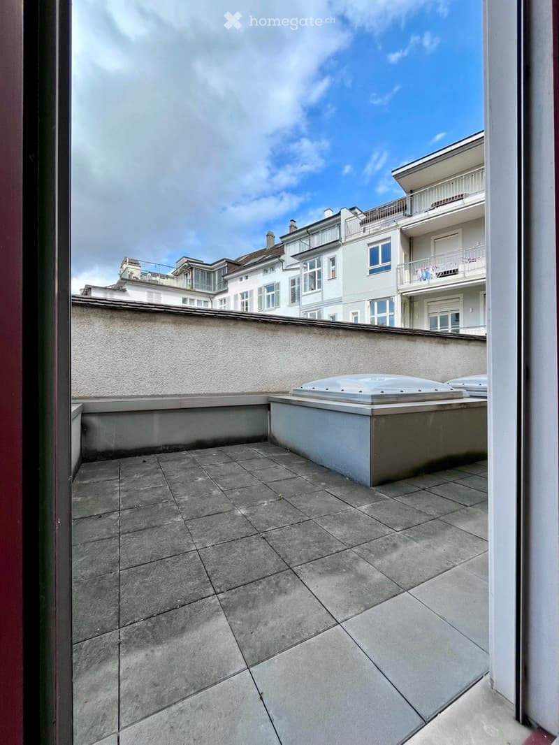 Roof terrace with tiled floor, small covered seating area, and view of neighboring buildings.