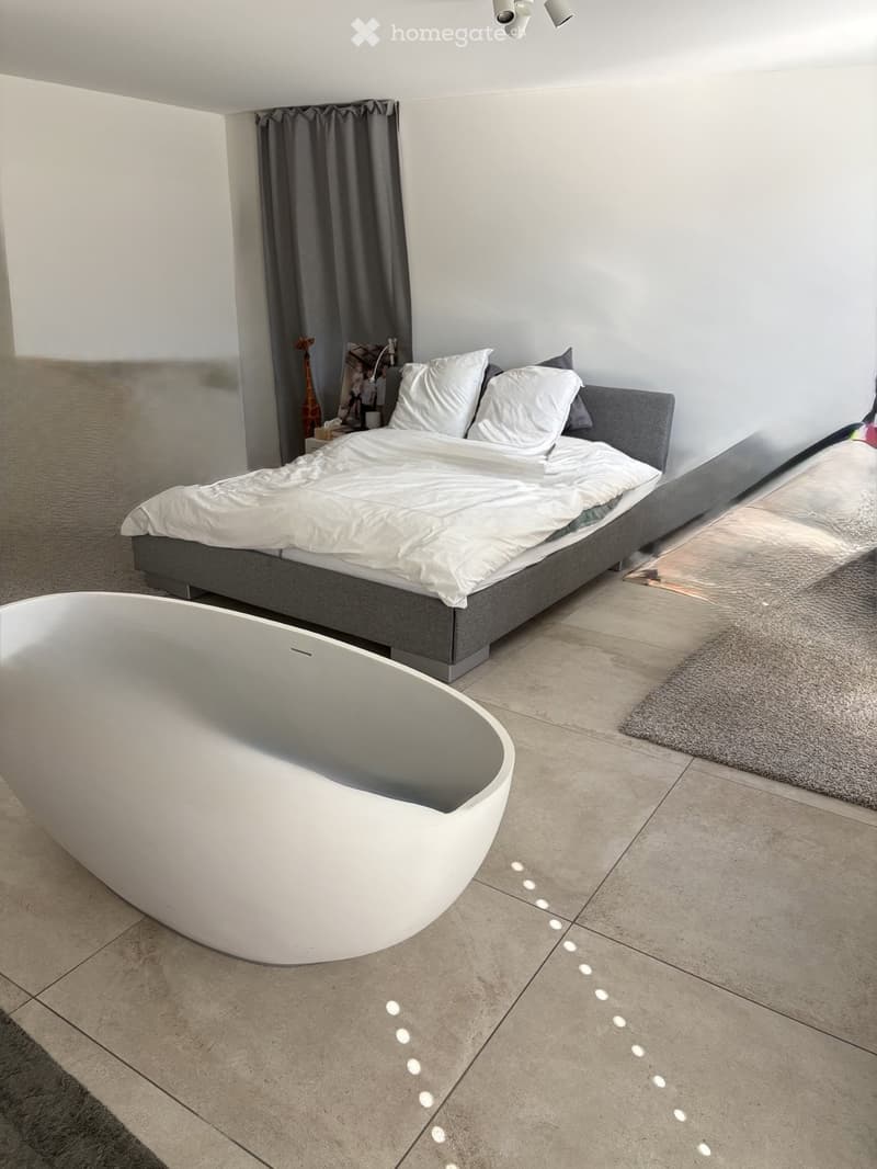 Modern bedroom with a large bed, white bedding, a sleek bathtub, and a gray rug on the floor.