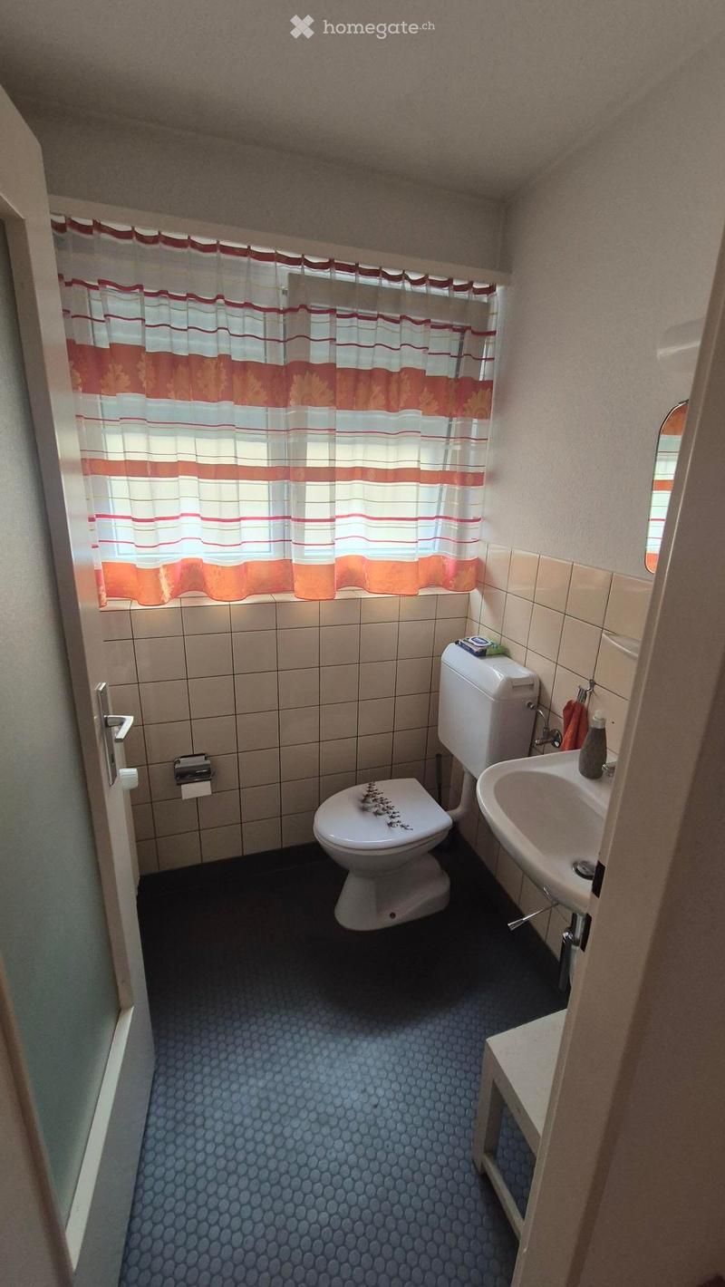 Small bathroom with a toilet, sink, and shower curtain. Blue patterned floor and beige tiled walls.