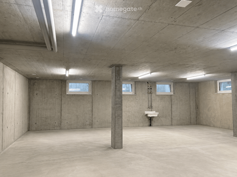 Empty underground parking space with concrete walls, floor, and ceiling, featuring a single sink and four small windows.