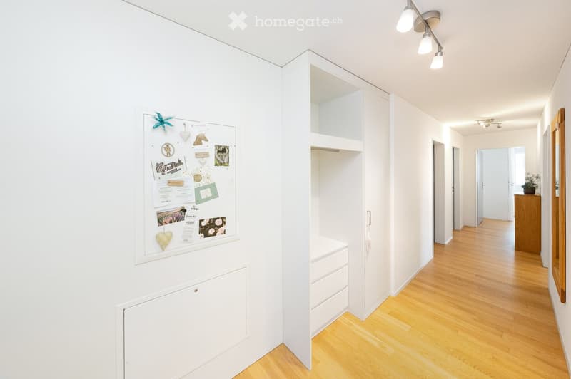 Bright hallway with white walls, wooden flooring, built-in storage unit, and a bulletin board with notes and decorations.