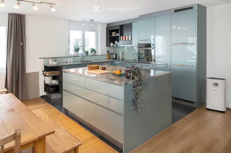 Modern kitchen with grey cabinets, granite countertop, stainless steel appliances, wooden dining table, and potted plants.