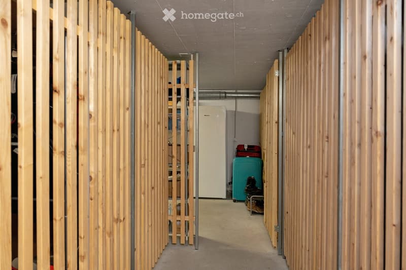 A narrow hallway with wooden paneling on both sides, featuring a small storage area with a refrigerator, suitcases, and shoes placed on the floor.