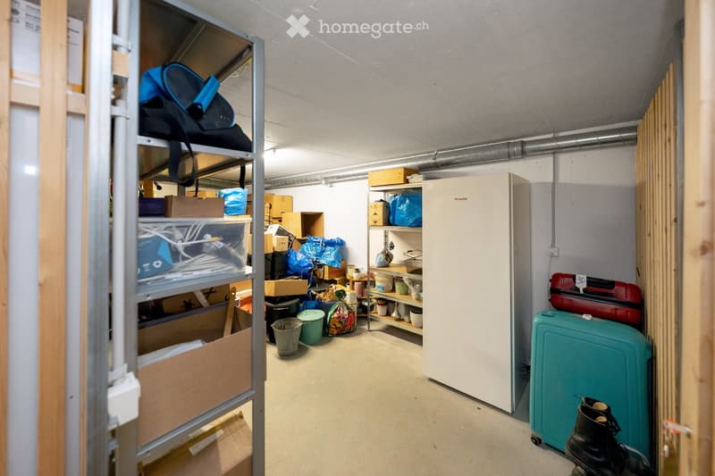 A storage room with a refrigerator, shelves filled with boxes and bags, a backpack, suitcases, and shoes on the floor.