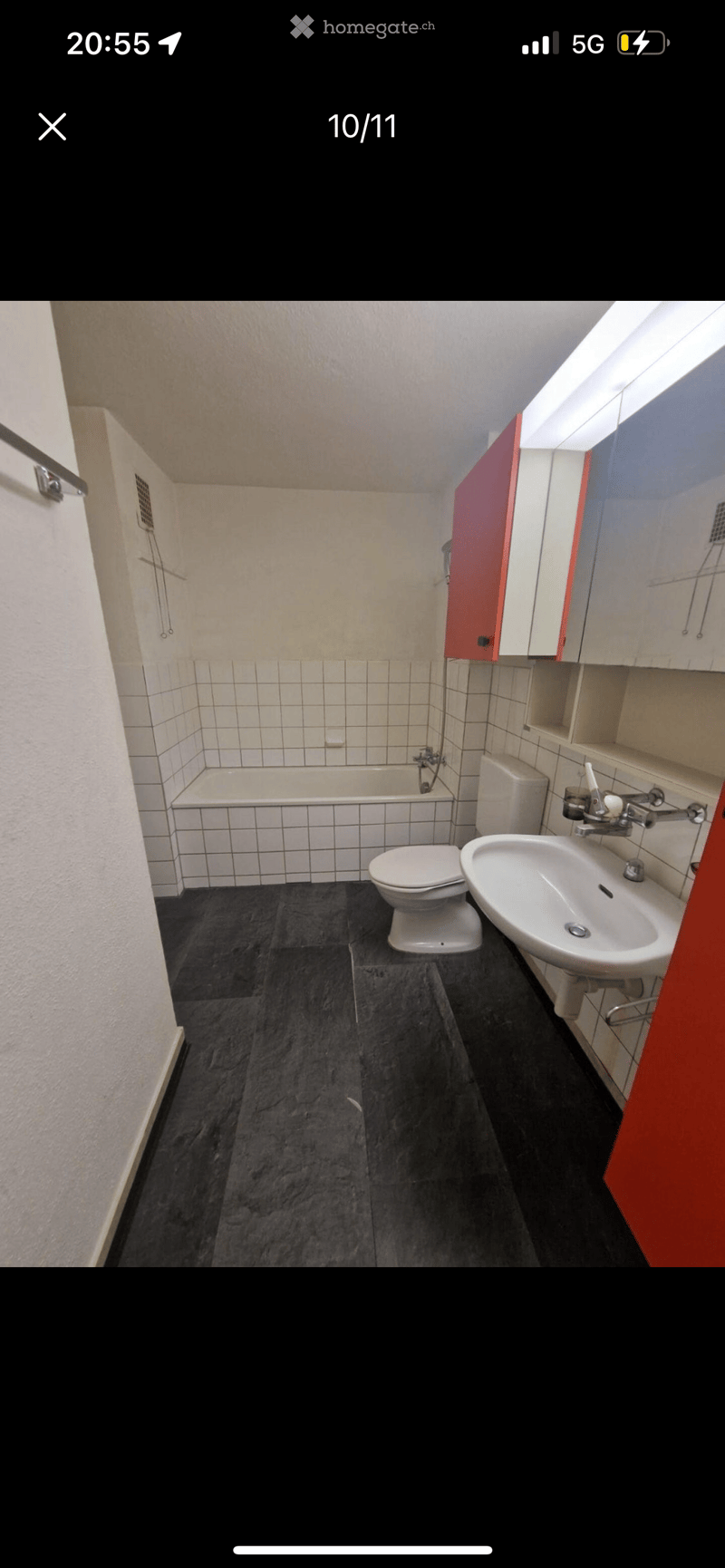Bathroom features a bathtub, toilet, and sink with cabinets, white tiled walls and floors, red cabinet, and ceiling light.