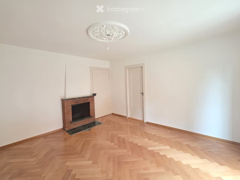 Empty room with wooden herringbone flooring, white walls, a brick fireplace, and two white doors.