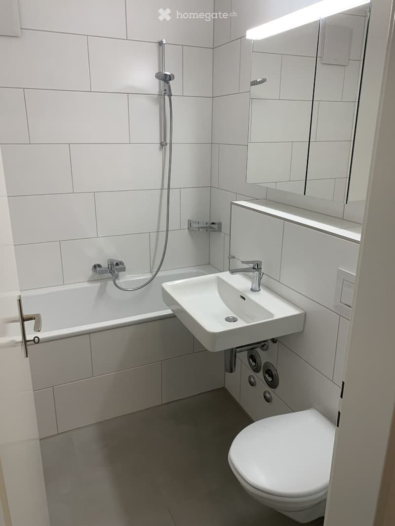 Modern bathroom with white tiles, a bathtub, a sink, a toilet, a mirror, and a showerhead.