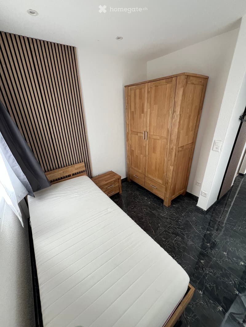 bed with mattress, wooden bed frame, wooden wardrobe with 3 drawers, side table with drawers, white walls, tiled floor