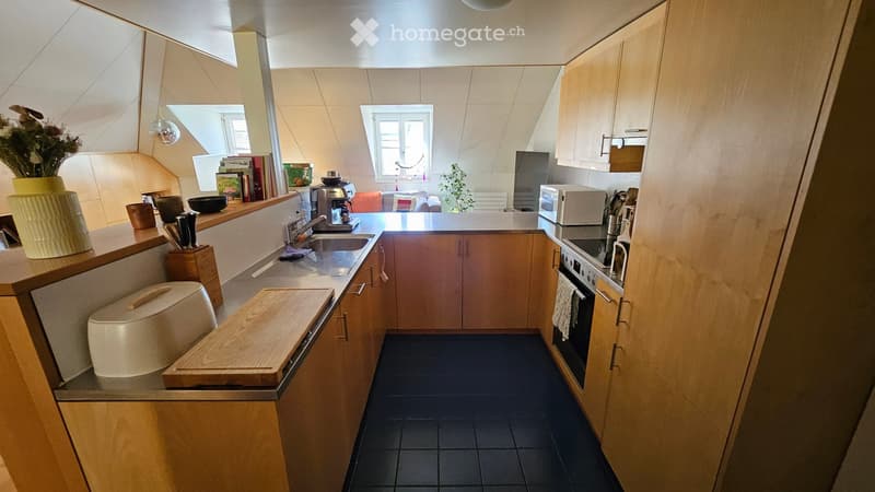 Modern kitchen with wooden cabinets, black tiled floor, and various appliances including a sink, oven, microwave, and coffee maker. There is a vase with flowers on the counter and a cutting board.