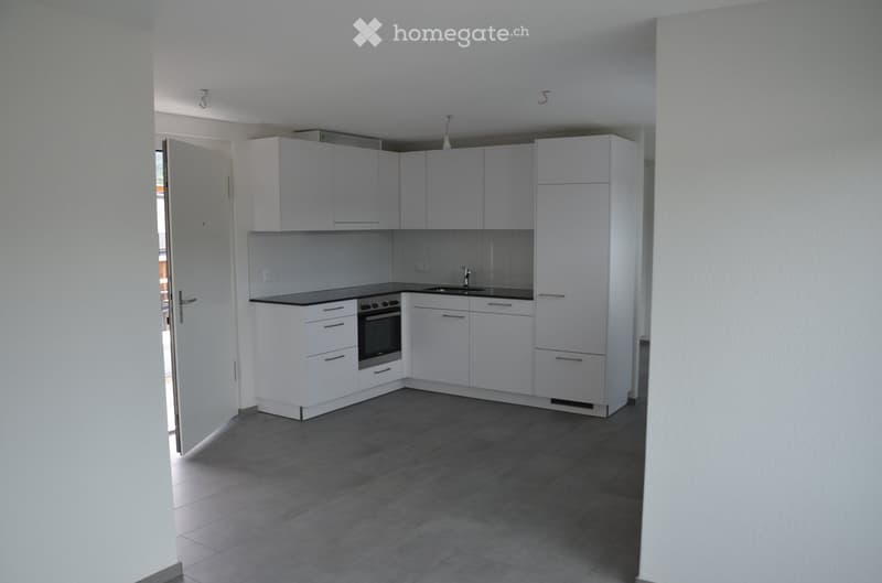 Modern kitchen with white cabinets, black countertops, and a built-in oven. The space features a dark tiled floor and a visible doorway leading to another room.