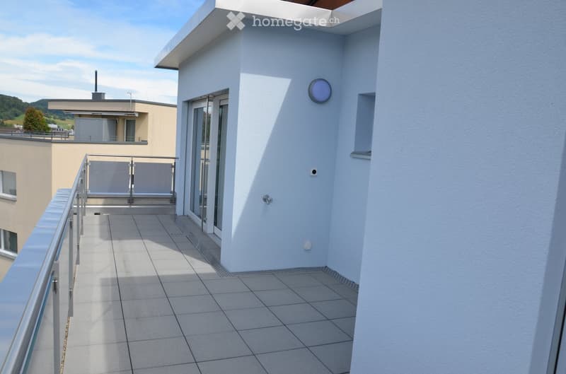 Modern balcony with tiled floor, metal railing, and glass door leading to the interior. The balcony has a clean, minimalist design with a round wall-mounted light fixture.