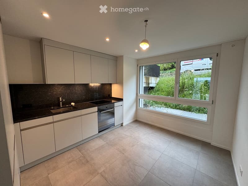Modern kitchen with white cabinets, black countertop, stainless steel sink, and built-in oven. Large window offers a view of greenery outside.