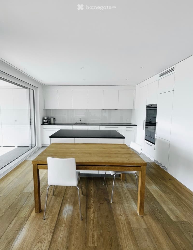 Modern kitchen with white cabinets, black countertop, wooden dining table, and white chairs.