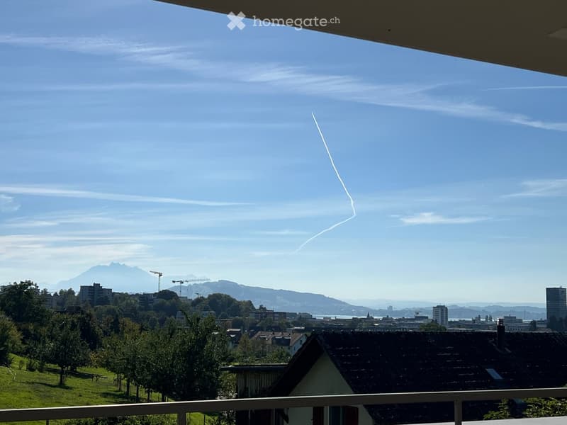 Balcony overlooking a cityscape with mountains in the background, clear blue sky, and visible construction cranes.