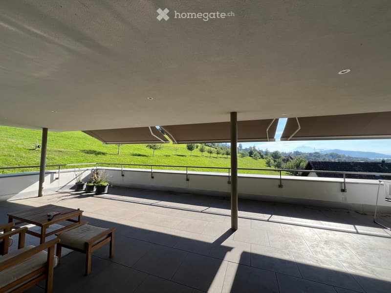 Balcony with tiled floor, wooden table, chairs, potted plants, and scenic view of green hills and mountains.