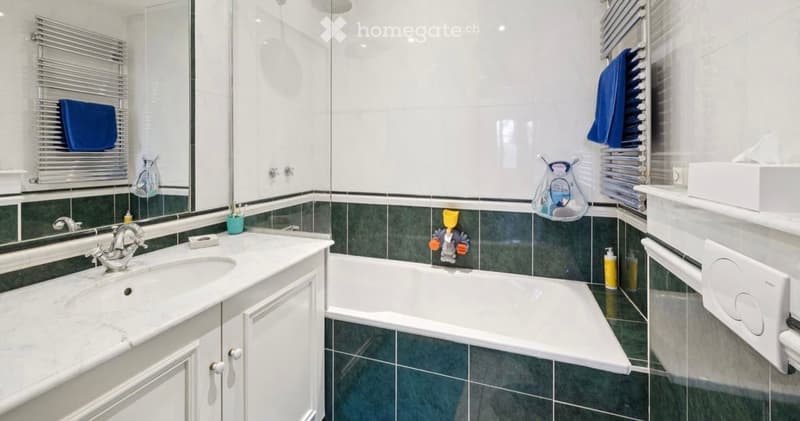 Modern bathroom with a white marble sink, chrome faucet, large mirror, bathtub, towel racks with blue towels, and a shower area with a glass enclosure.