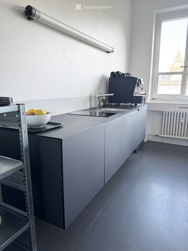 Modern kitchen with grey cabinets, a sink, a coffee machine, and a bowl of fruit on the counter.