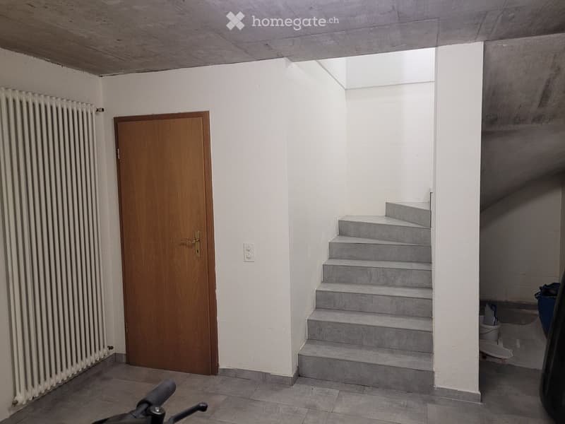 Empty hallway with a wooden door, radiator, and concrete staircase leading upwards.