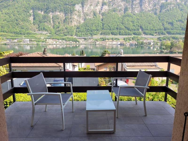 Balcony with two chairs and a small table, overlooking a scenic lake and town.