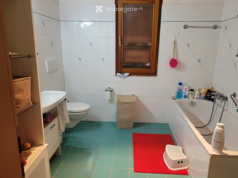 Bathroom with white tiles, blue floor tiles, sink, toilet, bathtub, towel, bath mat, and various toiletries.