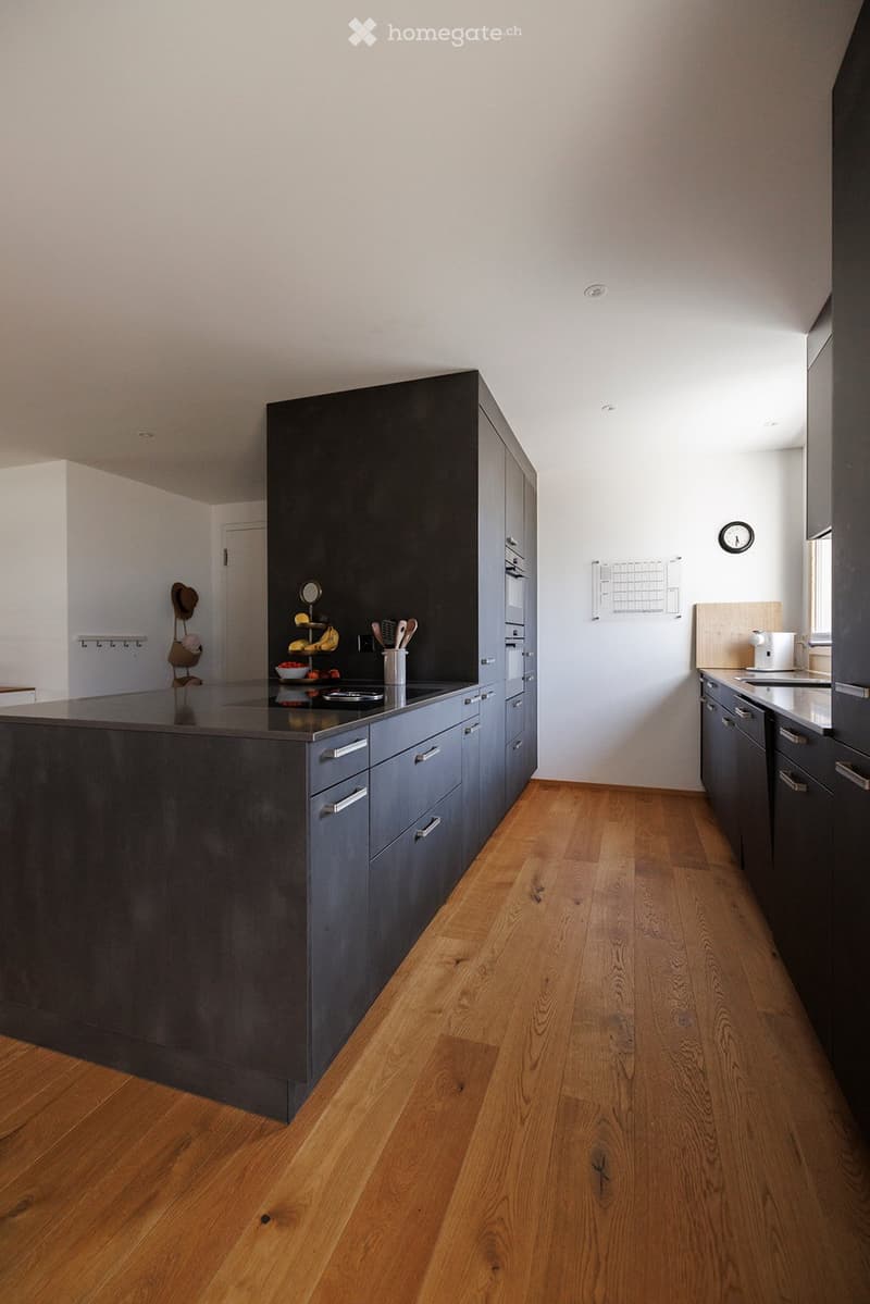 Modern kitchen with dark grey cabinets, a central island, wooden flooring, and various appliances and utensils.