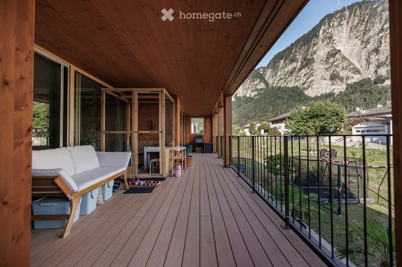 Wooden balcony with a sofa, small table, and chairs, overlooking a scenic mountain view.