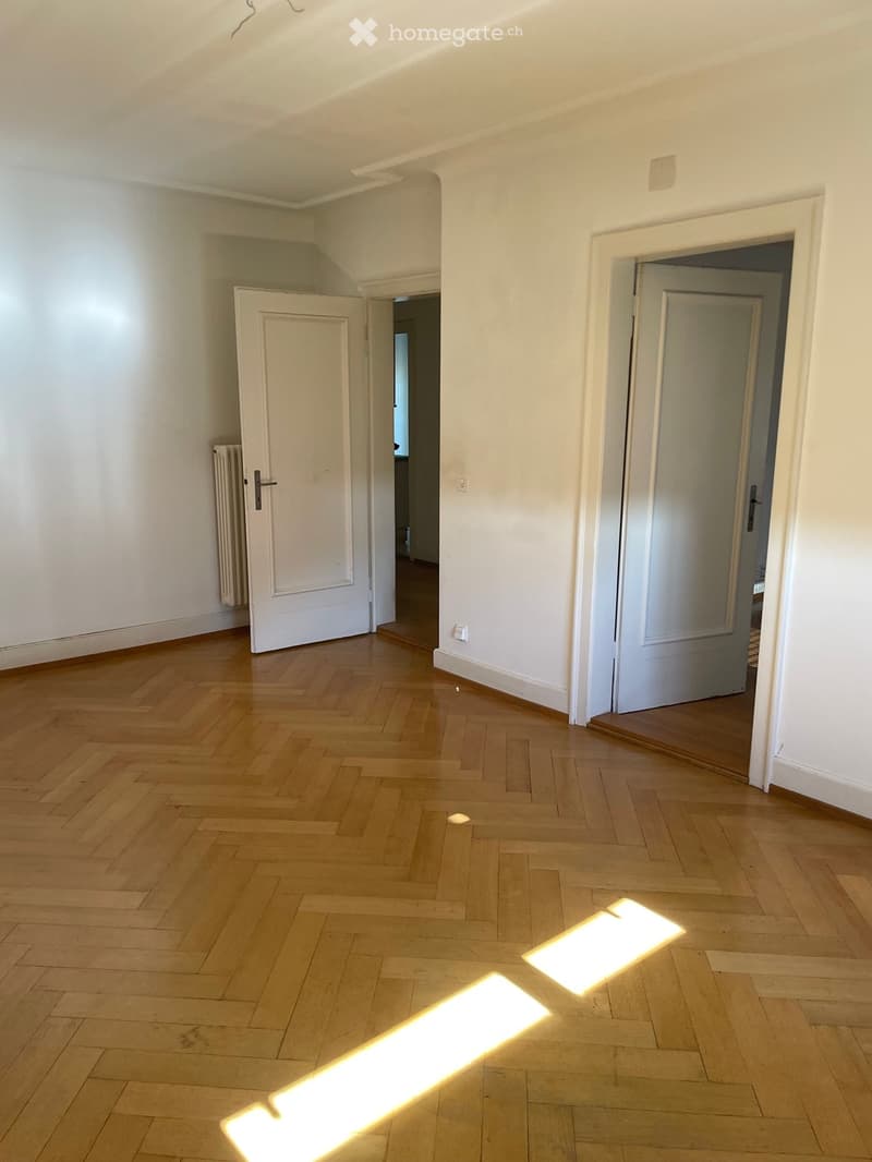 Empty room with wooden herringbone flooring, white walls, and two open doors leading to other spaces.