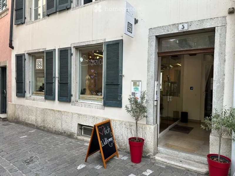 Facade of a building with a storefront, green shutters, a chalkboard sign, and potted plants.