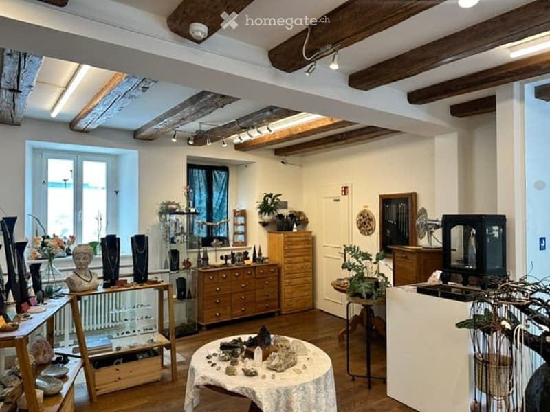 A well-lit room with exposed wooden beams, featuring a variety of decorative items including vases, plants, and a cabinet. The space is furnished with tables and chairs, creating a cozy and inviting atmosphere.
