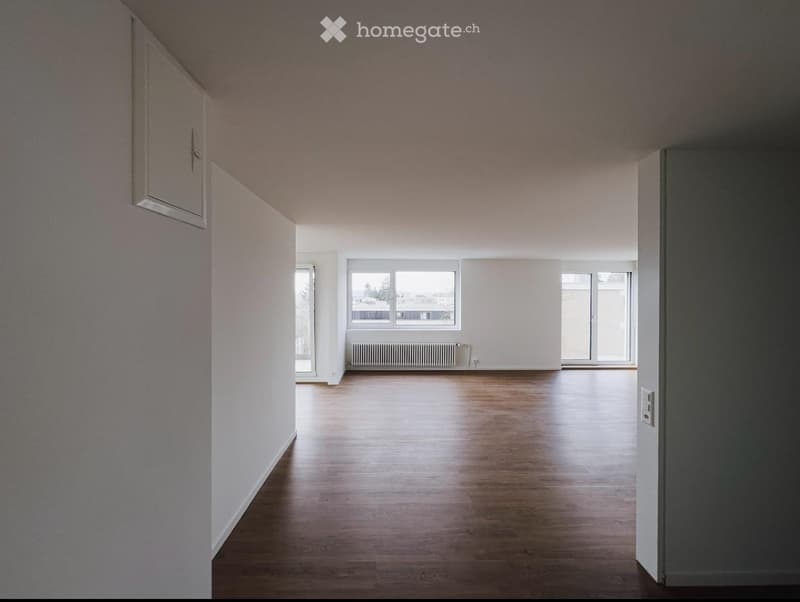 Empty room with wooden flooring, white walls, and large windows allowing natural light. No furniture or equipment present.