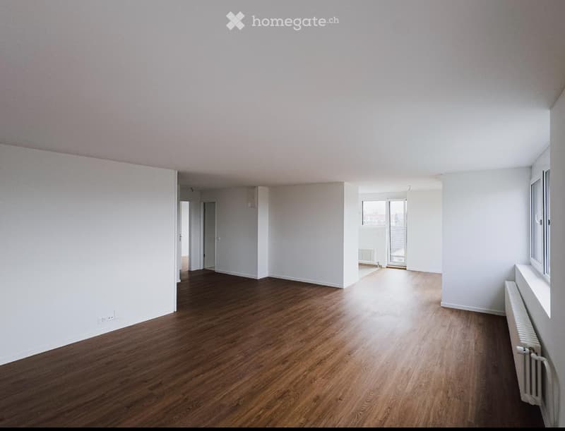 Empty room with wooden flooring, white walls, and large windows allowing natural light. No furniture or equipment is present.