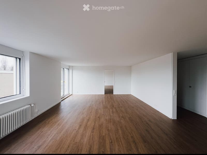 Empty room with wooden flooring, white walls, large windows, and a radiator. No furniture or equipment present.