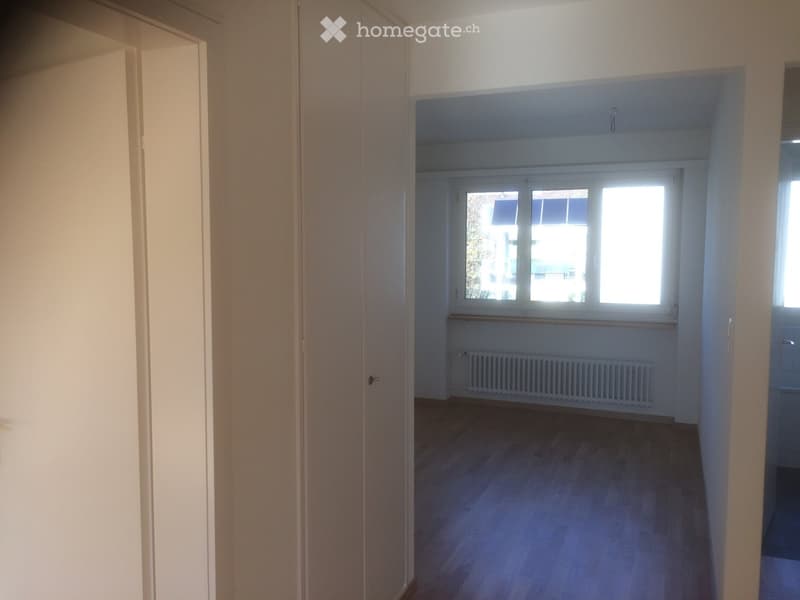 Empty room with wooden flooring, white walls, and a window with a radiator below it. No furniture or personal items are present.