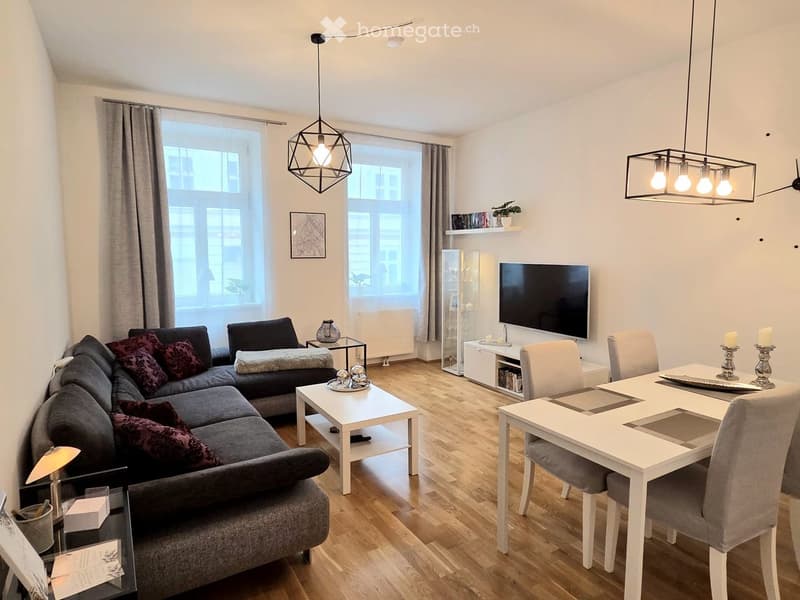 Modern living and dining area with a grey sectional sofa, coffee table, dining table with chairs, wall-mounted TV, and decorative items including candles and a picture frame.