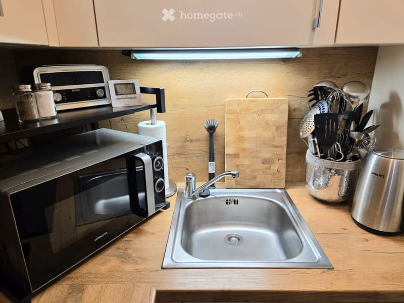 Modern kitchen with wooden countertops, stainless steel sink, microwave, and various kitchen utensils neatly arranged.