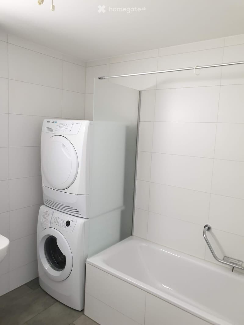 Bathroom with a bathtub, a washing machine, and a dryer stacked vertically.