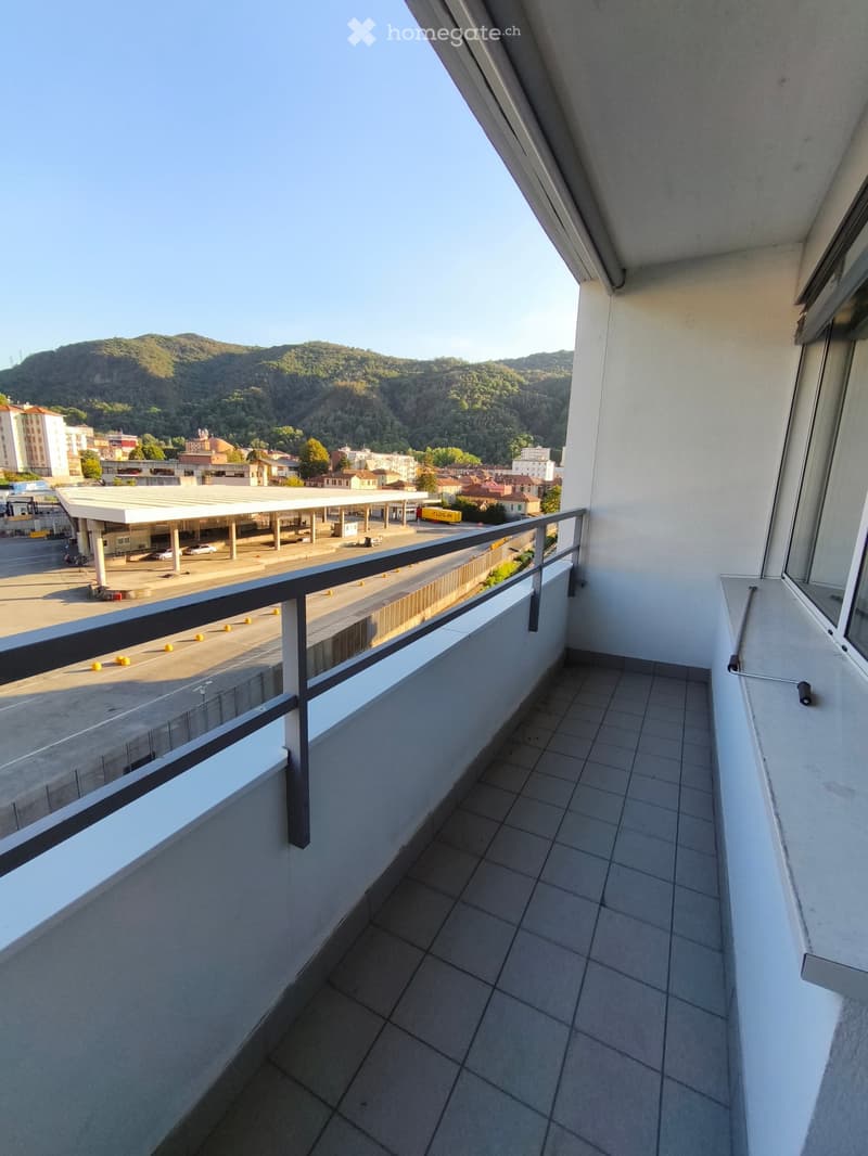 Balcony with tiled floor, metal railing, overlooking a cityscape and mountains.