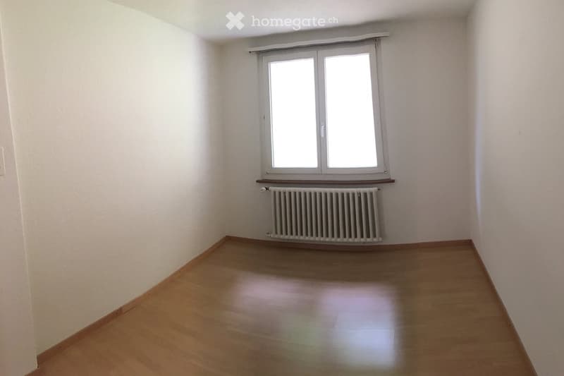Empty room with wooden flooring, white walls, a window with blinds, and a radiator below the window.