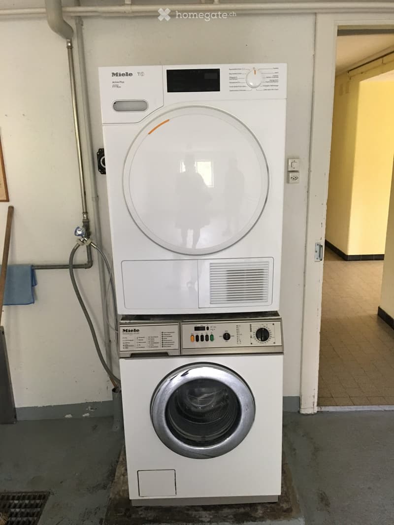 A private washing machine and dryer unit is installed in a hallway area with tiled flooring and white walls.